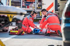 two men in orange jackets working on an emergency kit next to a firetruck