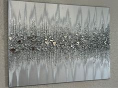 an abstract painting on the wall with silver and white colors, including small rocks in the middle