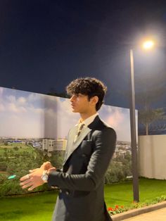 a man in a suit and tie standing next to a wall with a painting on it