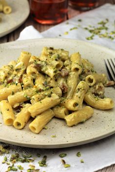 a white plate topped with pasta covered in sauce and nuts next to a fork on a table