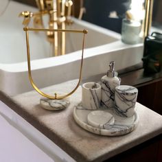 two marble cups and saucers on a tray in front of a bathtub with gold fixtures