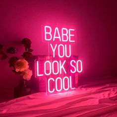 a neon sign that says babe you look so cool next to a vase with flowers