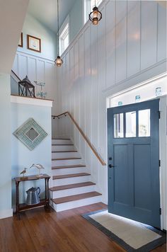 a blue door is in the middle of a wooden flooring area with white walls and stairs