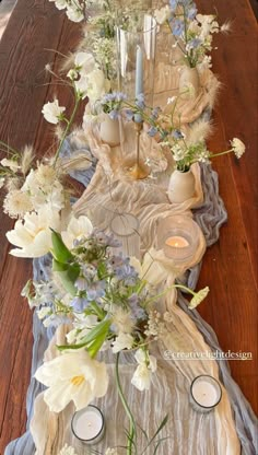 an arrangement of flowers and candles on a table with a cloth draped over the table