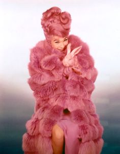 a woman in a pink fur coat sitting down