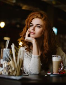 a woman sitting at a table with a drink in her hand and looking off to the side