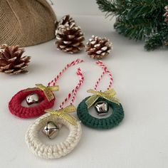 three christmas bells hanging from twine with pine cones in the background