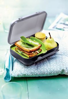 an open lunch box with sandwich, fruit and water on the table next to it