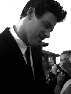 a man in a suit and tie looking at his cell phone while others look on