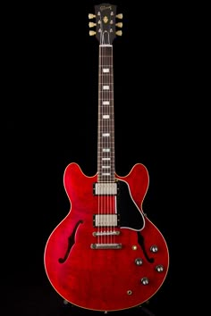 a red electric guitar sitting on top of a black surface with its neck up and head down