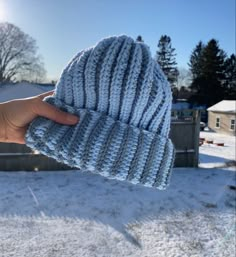 a hand holding up a blue knitted hat in the snow