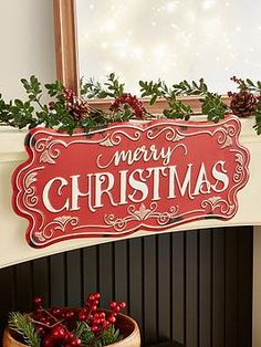 a red merry christmas sign hanging from the side of a fireplace with greenery on it