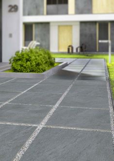 a concrete walkway in front of a building with grass and bushes on the side walk