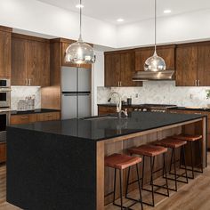 a kitchen with wooden cabinets and black counter tops next to an island that has four stools in front of it