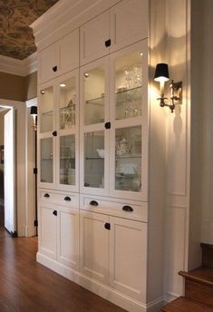 a white china cabinet with glass doors in the middle of a wooden floored hallway