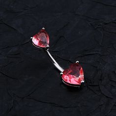 two heart shaped red stones are attached to a silver barbell ring on a black surface