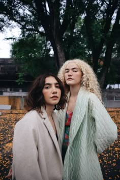 two women standing next to each other in front of trees