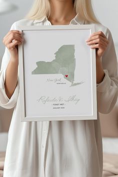 a woman holding up a framed map of the state of new york with her heart