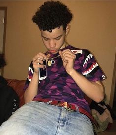 a young man sitting on top of a couch holding two cell phones