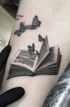 an open book with two butterflies flying out of it on the left side of the arm