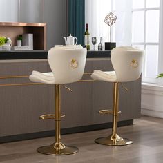 two white chairs sitting on top of metal stools in front of a kitchen counter