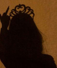 the shadow of a woman holding a knife in front of a wall with a crown on it