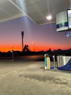 an empty gas station at sunset with the sun setting in the distance and no one around it