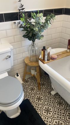 a white toilet sitting next to a bath tub in a bathroom under a plant on top of a wooden stand