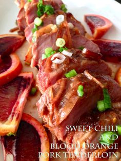 meat and blood orange slices on a white plate with green onion garnishes