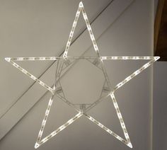 a lighted star hanging from the ceiling in front of a white wall with lights on it