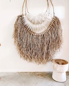 a woven bag hanging on the wall next to a white vase with a plant in it