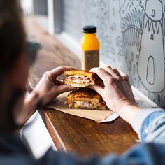 a person sitting at a table with a sandwich in front of him and a bottle of mustard