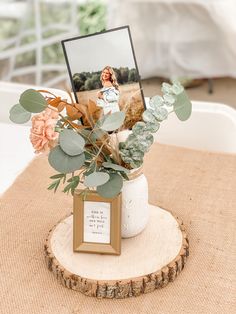 a vase filled with flowers and greenery on top of a wooden table next to a photo frame