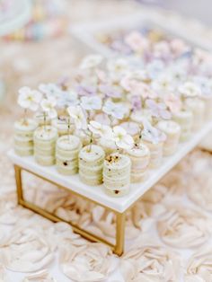 a table topped with lots of cupcakes on top of a white tray covered in flowers