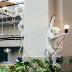 two white statues on the side of a building next to plants and potted plants