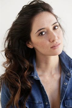 a woman with long dark hair wearing a denim shirt and looking off to the side