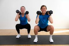 two women doing squats with dumbbells in front of them on a mat