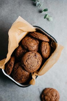 chocolate cookies in a metal container on a gray surface next to some leaves and flowers