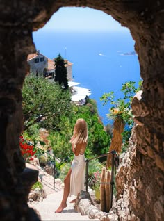 a woman in a white dress sitting on steps looking out at the ocean