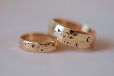 two gold wedding rings with stars and moon designs on the outside, set against a white background