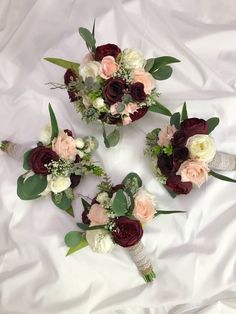 three bridal bouquets with roses and greenery laid out on a white sheet