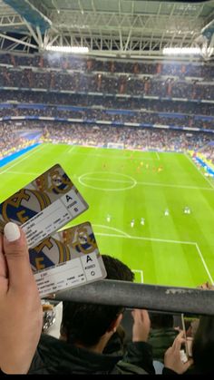 a person holding up two tickets in front of a stadium filled with people watching soccer