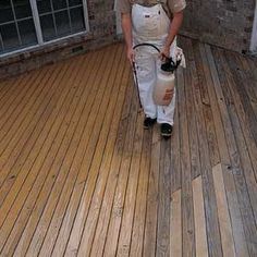 a man in white overalls holding a paint roller on a wooden floor next to a brick wall