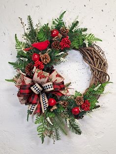 a christmas wreath hanging on the wall with pine cones, berries and evergreens around it