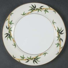 a white plate with green leaves and gold trimmings on the rim, against a black background