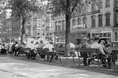 an old black and white photo of people sitting on park benches in the city street