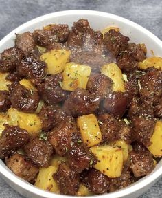 a white bowl filled with meat and potatoes covered in seasoning on top of a table