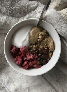 a bowl filled with cereal and berries on top of a white blanket next to a spoon