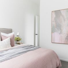 a bedroom with white walls, pink bedding and a large painting on the wall