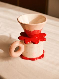 a white and red vase sitting on top of a bed next to a cup with a flower in it